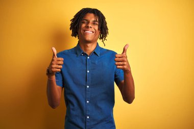 Rastgele kot gömlek giyen Afro bir adam izole edilmiş sarı arka plan başarısı tabelasının üzerinde duruyor. Elleriyle olumlu jest yapıyor, gülümsüyor ve mutlu. Neşeli ifade ve kazanan jest.