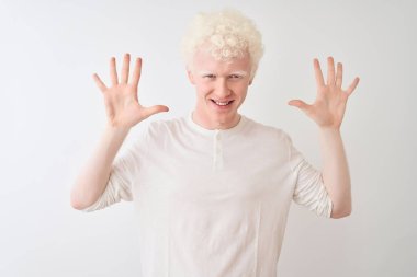 Genç albino sarışın adam, günlük tişörtler giyip izole edilmiş beyaz arka plan üzerinde duruyor ve parmaklarını on numarayı gösterirken kendinden emin ve mutlu bir şekilde gülümsüyor..