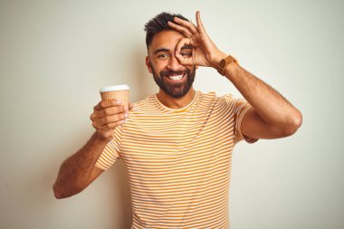 Genç Hintli bir adam, izole edilmiş beyaz arka planda durup kahve içiyor, gülümsüyor ve el pençe divan duruyor.