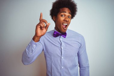İzole edilmiş beyaz arka plan üzerinde çizgili gömlek ve mor papyon takan afro iş adamı başarılı bir fikirle parmağı işaret ediyor. Heyecanlı ve mutlu. Bir numara..