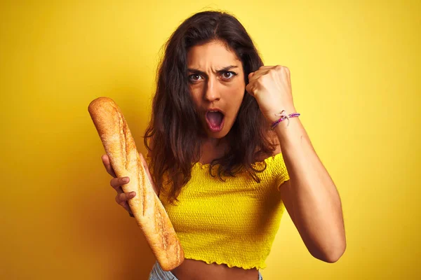 孤立した黄色の背景に立ってパンを保持若い美しいパン屋の女性がいらいらし 怒りで叫んで 狂気と大声で手を上げ 怒りの概念 — ストック写真