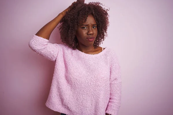 Young african afro woman wearing sweater standing over isolated pink background confuse and wonder about question. Uncertain with doubt, thinking with hand on head. Pensive concept.