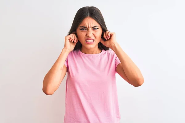 ピンクのカジュアルなTシャツを着た若い美少女が 白い背景に耳を指で覆い 大きな音楽のノイズに悩まされる表情で立っている ろう者の概念 — ストック写真