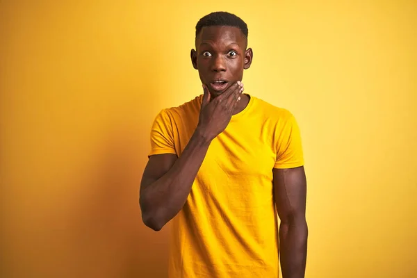 孤立した黄色の背景の上に立ってカジュアルなTシャツを着て若いアフリカ系アメリカ人の男顎に手で不信感 驚きと驚きの表現に魅了見て — ストック写真
