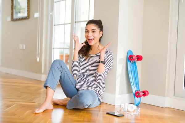 年轻女子坐在地板上 用滑板和耳机庆祝疯狂和惊奇的成功 举臂和睁开眼睛尖叫兴奋 赢的概念 — 图库照片