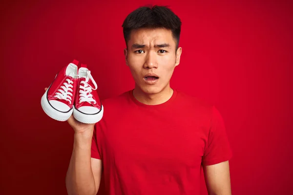 Молодий Азіат Який Тримає Випадкові Кросівки Стоячи Над Ізольованим Червоним — стокове фото