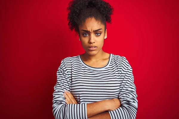 African american woman wearing navy striped t-shirt standing over isolated red background skeptic and nervous, disapproving expression on face with crossed arms. Negative person.