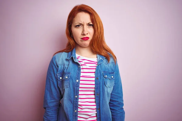 Beautiful redhead woman wearing denim shirt and striped t-shirt over isolated pink background skeptic and nervous, frowning upset because of problem. Negative person.