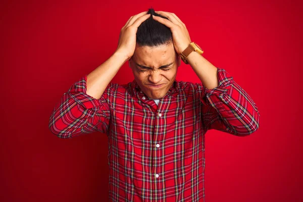 Genç Brezilyalı gömlekli adam izole edilmiş kırmızı arka planda dikiliyor. Ağrı ve migren yüzünden baş ağrısı ve stresten muzdarip. Ellerini başının üstüne koy..