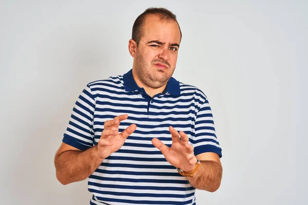 Young man wearing casual striped polo standing over isolated white background disgusted expression, displeased and fearful doing disgust face because aversion reaction. With hands raised. Annoying concept.