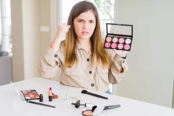 Beautiful young woman using make up cosmetics applying color from palete annoyed and frustrated shouting with anger, crazy and yelling with raised hand, anger concept
