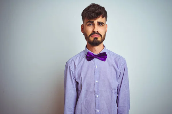 Young man with tattoo wearing purple shirt and bow tie over isolated white background depressed and worry for distress, crying angry and afraid. Sad expression.