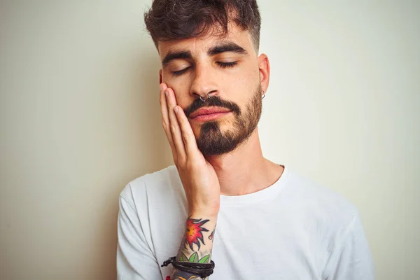 Young man with tattoo wearing t-shirt standing over isolated white background thinking looking tired and bored with depression problems with crossed arms.