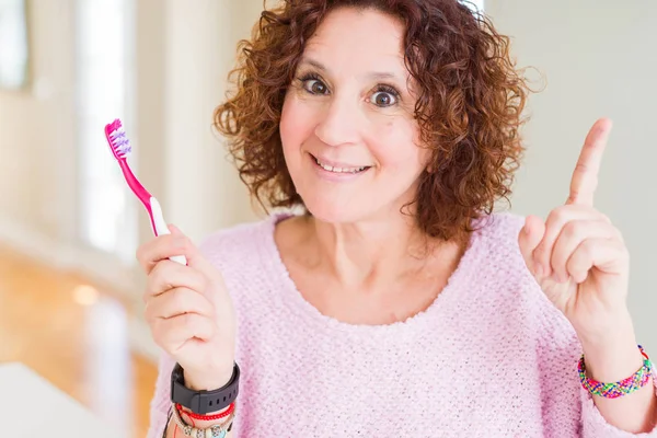 Starsza Kobieta Trzymająca Różową Szczoteczkę Zębów Klinice Stomatologicznej Zaskoczona Pomysłem — Zdjęcie stockowe