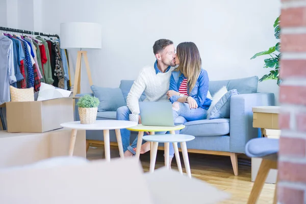 Genç güzel çift karton kutular etrafında yeni evde dizüstü bilgisayar kullanarak kahve kanepede içme fincan oturan