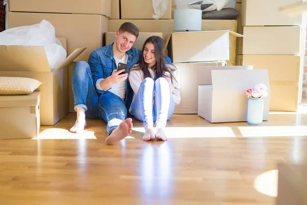 Pareja joven sentada en el suelo de una casa nueva alrededor de cartón — Foto de Stock