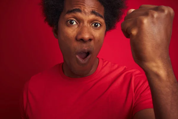 孤立した赤い背景に立っているTシャツを着てアフロの髪を持つ若いアメリカ人男性は 怒りとイライラ叫び 狂気と大声で手を上げ 怒りの概念 — ストック写真