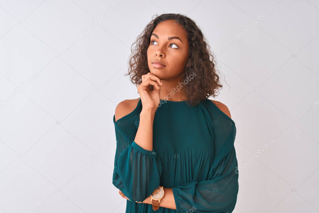 Young brazilian woman wearing green t-shirt standing over isolated white background with hand on chin thinking about question, pensive expression. Smiling with thoughtful face. Doubt concept.