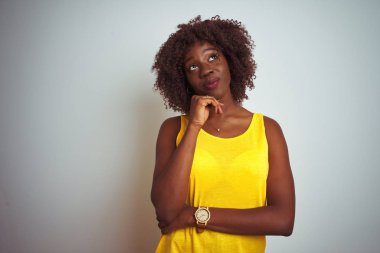 İzole edilmiş beyaz arka planda sarı tişört giyen Afrikalı genç bir kadın. Elleri çenesinde soru sorarken, düşünceli bir ifade takınıyor. Düşünceli bir yüzle gülümsüyor. Şüphe kavramı.