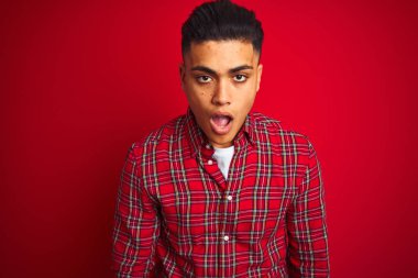 İzole edilmiş kırmızı arka planın üzerinde dikilen Brezilyalı genç adam korku, korku ve heyecan dolu yüz ifadesiyle dehşete düşmüş ve şok olmuştu..