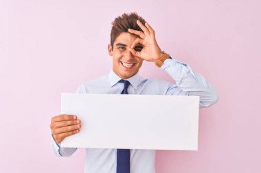 Genç yakışıklı iş adamı, pembe arka planda tek başına durmuş mutlu yüzüyle afiş tutuyor. Tamam işareti yapıyor, parmaklarından bakıyor.