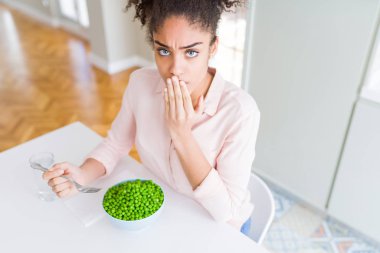 Afro-Amerikalı genç bir kız sağlıklı yeşil bezelye yiyerek ağzını kapatıyor. Utanç verici bir hata, korku ifadesi, sessizlikten korkmak, gizli bir kavram.