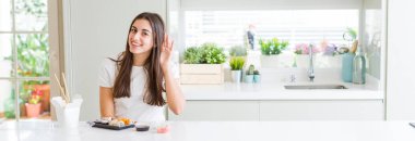 Asya suşisi yiyen güzel bir kadının geniş açılı fotoğrafı. Kulaktan kulağa gülümseyen bir şekilde söylenti ve dedikoduları dinliyor. Sağırlık kavramı.