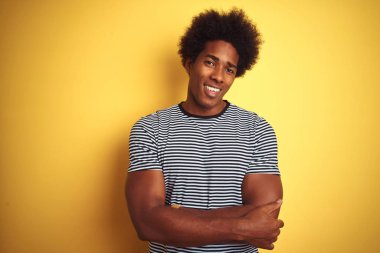 Afro saçlı, donanma çizgili tişörtlü, izole edilmiş sarı arka plan mutlu yüzlü, kollarını kavuşturup kameraya bakan Afro-Amerikan bir adam. Pozitif kişi.