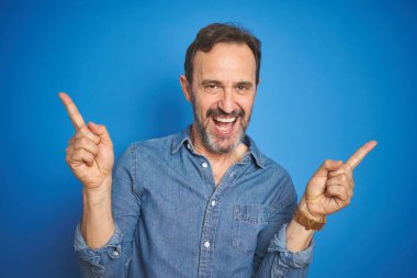 Yakışıklı, orta yaşlı, gri saçlı, mavi arka planda, kendine güvenen, parmaklarını farklı yönlere çeviren yaşlı bir adam. Reklam için boşluk kopyala