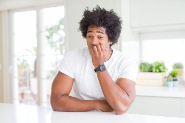 Beyaz günlük tişörtler giyen Afro-Amerikalı genç bir adam evde oturmuş gergin ve gergin görünüyor, elleri ağızdan tırnak yiyor. Endişe sorunu.