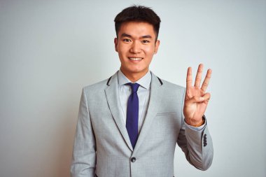 Asyalı Çinli işadamı takım elbise ve kravat takıp izole edilmiş sarı arka planda duruyor ve üç numaralı parmaklarıyla işaret ederken kendinden emin ve mutlu gülümsüyor..