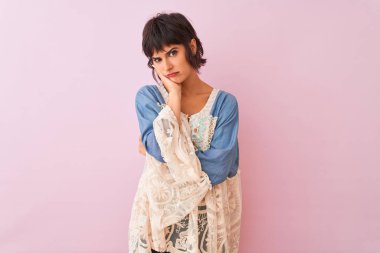 İzole edilmiş pembe arka planda dikilen rahat giyinen genç ve güzel bir kadın kollarını kavuşturarak depresyondan sıkılmış ve yorgun görünüyor..