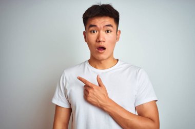 Asyalı, tişörtlü genç bir adam izole edilmiş beyaz arka planda dikiliyordu. Parmakla yüzünü gösteriyordu, ağzı açık şaşkın bir şekilde..