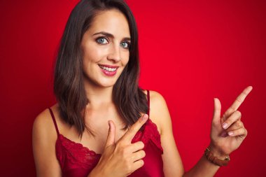 Genç güzel kadın kırmızı izole arka plan üzerinde seksi iç çamaşırı giyen gülümseyerek ve yan iki el ve parmak ile işaret kamera bakıyor.