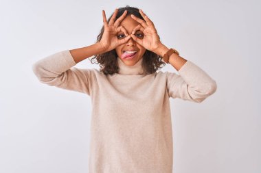 Balıkçı yaka kazak giyen genç Brezilyalı bir kadın izole edilmiş beyaz arka planda dikiliyor. Dürbün gibi jest yapıyor. Dürbün dilini çıkarıyor, gözler parmaklarından bakıyor. Çılgın ifade.