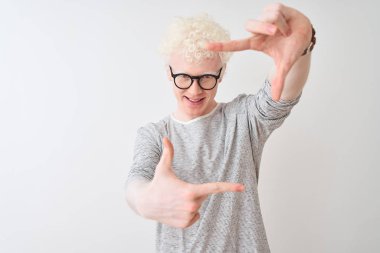 Genç, sarışın, çizgili tişört ve gözlük takan izole edilmiş beyaz arka planda gülümseyen, elleri ve parmakları mutlu yüzlü genç bir adam. Yaratıcılık ve fotoğrafçılık kavramı.