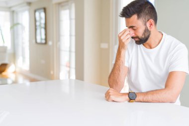 Yakışıklı, İspanyol asıllı, sıradan, beyaz tişörtlü, burnu ve gözleri ovuşturmaktan yorgun, yorgun ve başı ağrıyor. Stres ve hüsran kavramı.