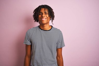 Siyah saçlı, denizci çizgili tişörtlü bir Afro adam pembe arka planda mutlu ve havalı bir gülümsemeyle dikiliyor. Şanslı kişi..