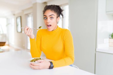 Genç Afro-Amerikan kadın sağlıklı yeşil sebzeler yiyor. Şaşırmış bir yüz ifadesinden korkuyor ve heyecanlanıyor.