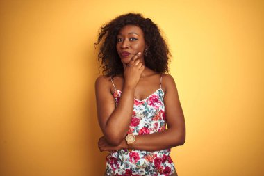 Sarı arka planda çiçekli tişört giyen Afro-Amerikalı bir kadın kameraya kollarını kavuşturup, elleriyle çenesini kaldırarak gülümsüyor. Olumlu düşünüyorum..