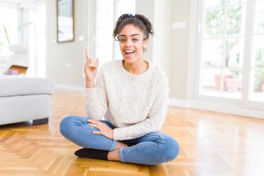 Yüzünde kocaman bir gülümseme ile katta oturan afro saçlı güzel genç Afro-Amerikan kadın kameraya bakarak yan el ve parmak ile işaret.