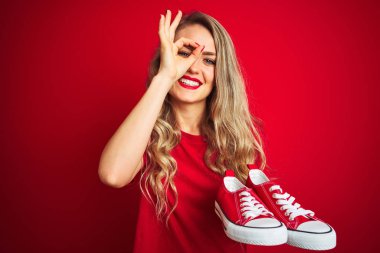 Güzel bir kadın kırmızı izole edilmiş arka planda moda ayakkabıları tutuyor. Mutlu bir yüzü var. Gülümsüyor.