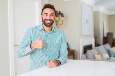 Yakışıklı İspanyol adam evde el ile jest kadar mutlu başparmak yapıyor. Başarı göstererek kameraya bakan ifadeyi onaylama.