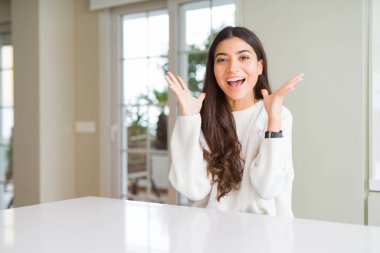 Genç güzel kadın evde beyaz masada deli kutluyor ve kollarını kaldırdı ve açık gözleri heyecan çığlık ile başarı için hayran. Kazanan kavramı