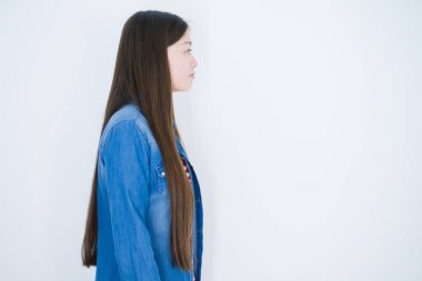 Güzel, genç Asyalı bir kadın, beyaz, soyutlanmış bir arka planda, yan tarafa bakıyor, rahat bir poz veriyor, kendine güvenen bir gülümsemeyle doğal bir yüz..