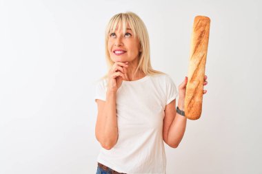 Orta yaşlı fırıncı kadın izole edilmiş beyaz arka planda duran ekmeği tutuyor. Ciddi bir yüz ifadesi var. Soru sormayı düşünüyor.