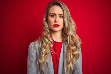 Kırmızı izole edilmiş arka planda duran zarif ceketli genç ve güzel bir iş kadını yüzünde ciddi bir ifadeyle rahatlamış. Basit ve doğal bir şekilde kameraya bakıyorsun..