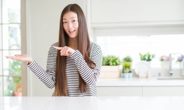 Güzel Asyalı kadın çizgili kazak giyen şaşırttı ve el ile sunarken kameraya gülümseyerek ve parmak ile işaret.