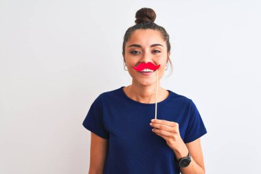 Genç, güzel bir kadın, kıç partisi bıyığını izole edilmiş beyaz arka planda tutuyor. Mutlu bir yüzü var, gülümsüyor ve kendine güvenen bir gülümsemeyle dişlerini gösteriyor.