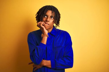 Rasta giyen, sarı arka planda mekanik üniforma giyen Afro işçi elleri ağız yiyen çivilerle gergin ve stresli görünüyor. Endişe sorunu.